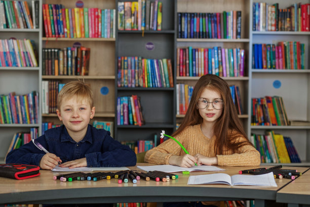 两个小学生坐在图书馆的桌子旁写字画画。同学们在教室里学习。图片下载