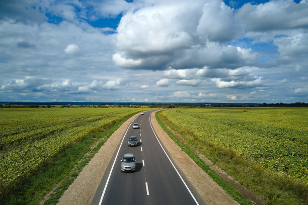 快速行驶的汽车在绿色农田之间的城际道路鸟瞰图。从无人机俯瞰高速公路交通图片下载