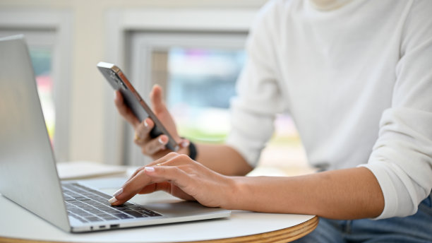 裁剪图像的女性远程工作在咖啡馆，使用笔记本电脑和她的手机。图片下载