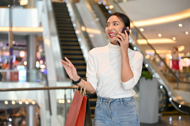 一名快乐的亚洲女子在商场购物时和她的朋友打电话。图片下载