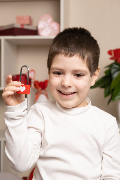 一个5岁的可爱男孩用他的心拿着一把锁，微笑着。情人节和孩子，初恋，学龄前儿童图片下载
