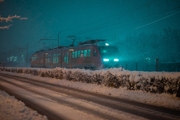 欧洲风格的红色通勤列车在大雪纷飞的夜晚飞驰而过。冬季乘火车安全出行的概念。图片下载