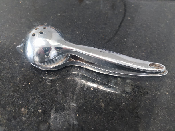 一个不锈钢柠檬榨汁机在黑色大理石表面上喷射图片下载