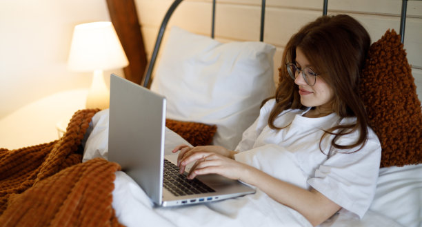 年轻有魅力的女人在家里床上的笔记本电脑工作的肖像。图片下载