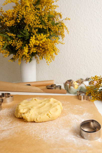 新鲜的面团在烘焙纸上，背景是一个花瓶和一束含羞草图片下载