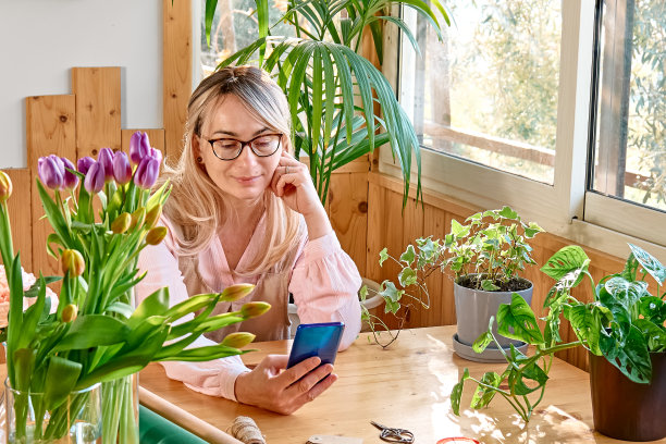 花店女花匠用智能手机接单。花交付。小型企业的社交媒体。图片下载