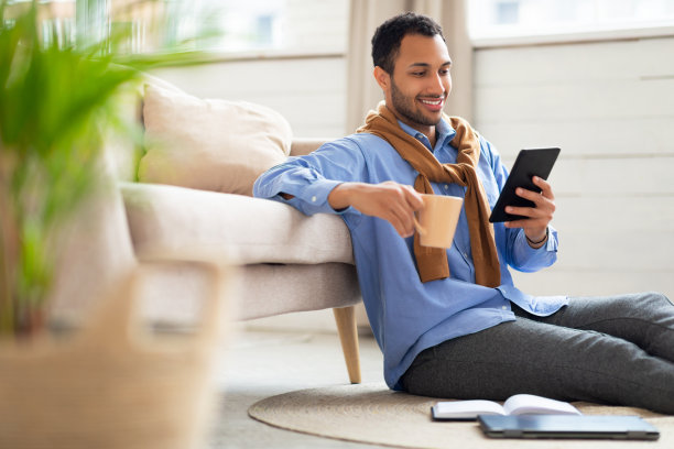 微笑的阿拉伯男子在平板电脑上看视频，喝咖啡图片下载