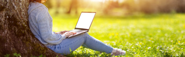 一个女人拿着笔记本电脑坐在自然公园的草地上。图片下载