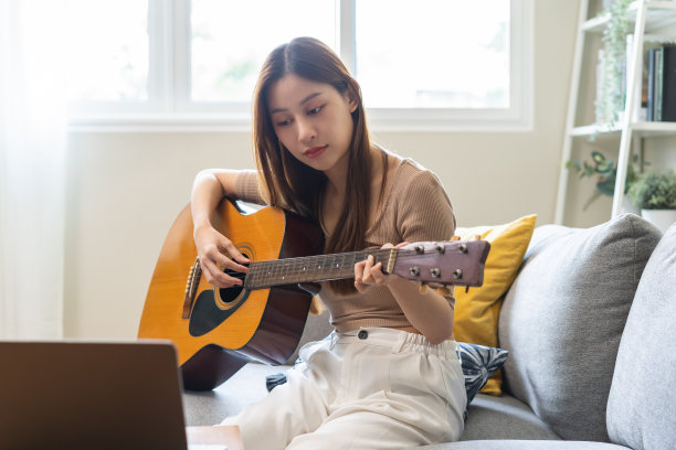 爱好放松的概念，快乐的亚洲年轻女子在休闲服装，弹原声吉他与笔记本电脑，学习玩在线课程，坐在沙发上在客厅，在家娱乐图片下载
