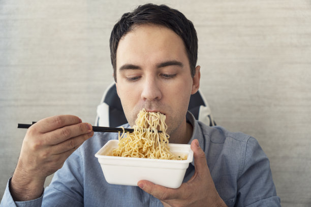 一名男子在办公室边吃方便面边工作。在办公室吃午餐。垃圾食品图片下载