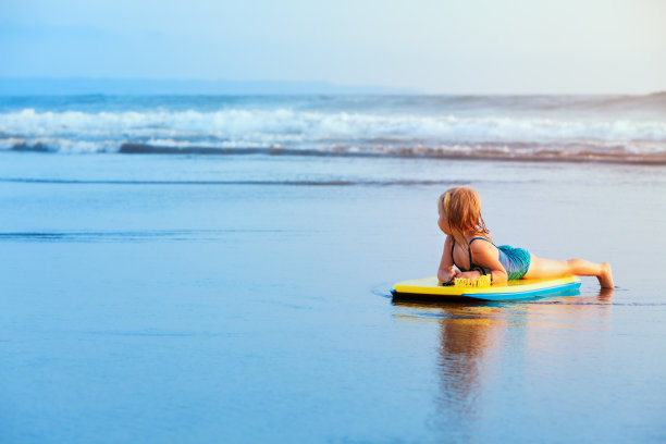 年轻的冲浪女孩带着冲浪板在海滩上玩图片下载