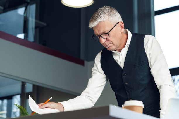 在办公室办公桌前工作的成熟商人。图片下载