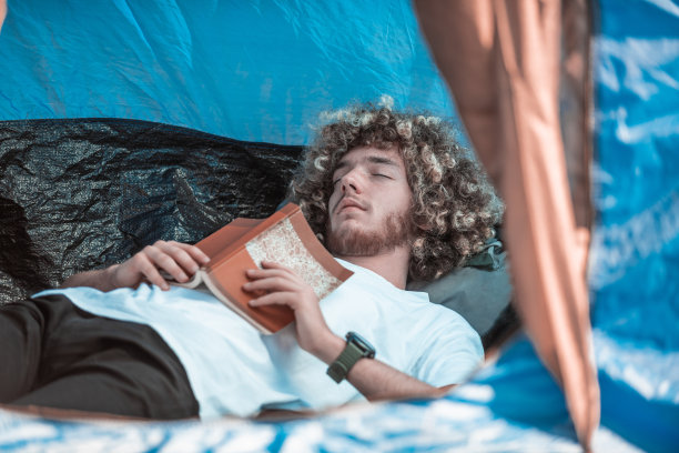 一个留着爆炸头的少年在登山帐篷里看书图片下载