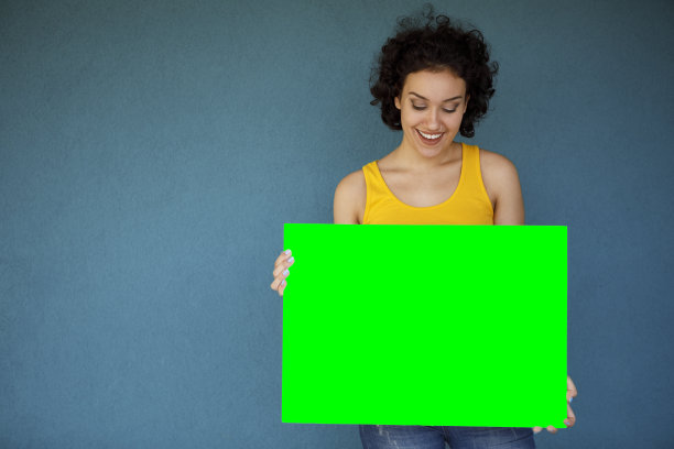 年轻女子拿着蓝色背景的空白绿色广告牌图片下载