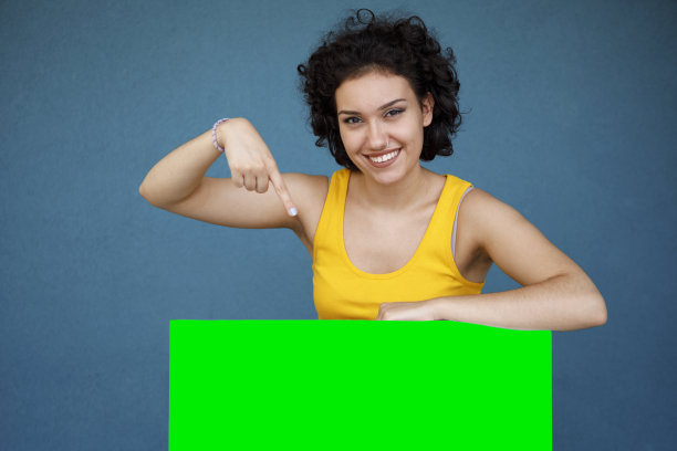 年轻女子指着蓝色背景下空白的绿色广告牌图片下载