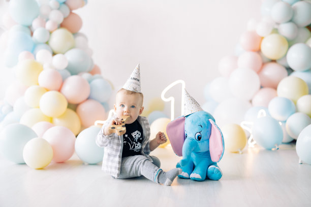 小男孩坐在气球和玩具大象旁边的地板上，庆祝它的一岁生日。图片下载