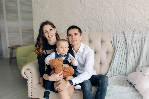 快乐的父母和他们蹒跚学步的儿子坐在沙发上。图片下载