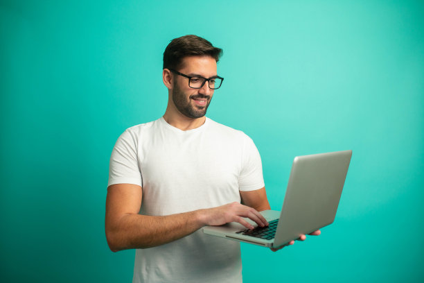 英俊的男子与眼镜在白衬衫拿着笔记本电脑，工作室肖像在蓝色的背景图片下载