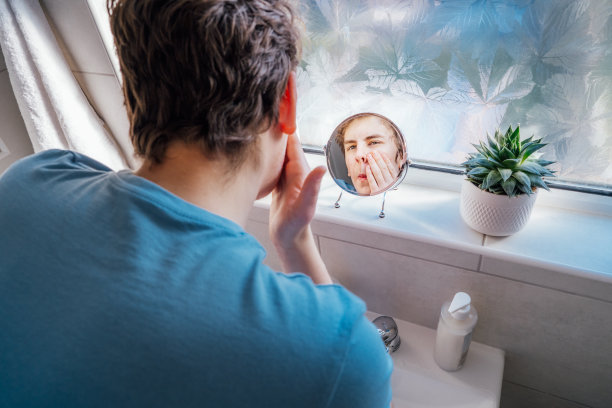 有痤疮问题的白人青少年集中在家照顾他的面部皮肤。他在浴室里对着镜子用洗液洗脸。青少年护肤流程图片下载