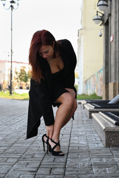 一个自信的年轻迷人的女人穿着黑色连衣裙和高跟鞋走在城市的街道上，女人微笑着享受生活图片下载