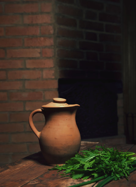 木桌上放着一个老式的乡村酒壶。陶土陶罐。构图中充满了绿色植物。体现民族色彩的概念照片。深色的背景，大量的广告空间图片下载