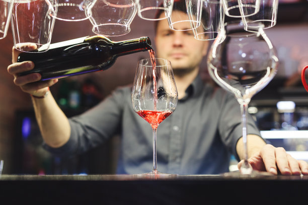 在昏暗的酒吧里，一名男子将红酒倒进玻璃杯图片下载