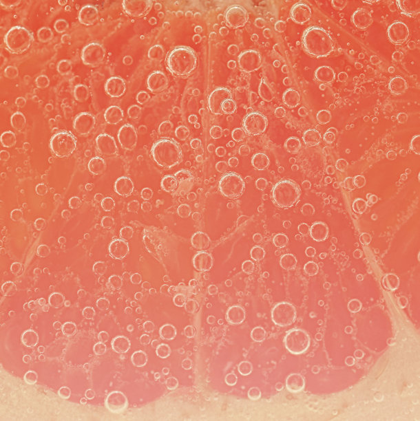 柚子片的特写与气泡的液体。将红熟葡萄柚切片放入水中。被气泡覆盖的新鲜葡萄柚片的特写图片下载