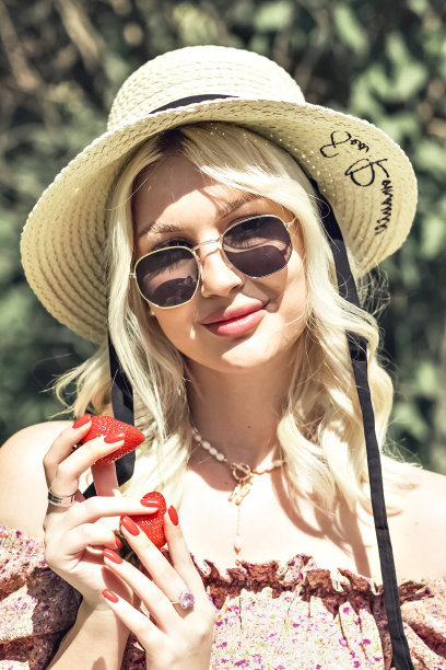 一个迷人的漂亮可爱的金发女士的照片，她手里拿着一个草莓。户外休闲，夏日野餐图片下载