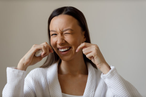 年轻女子淋浴后从事日常程序的肖像。刷牙，用牙线清洁牙齿。雪白的微笑，眨着眼睛。关爱、美丽、健康。图片下载
