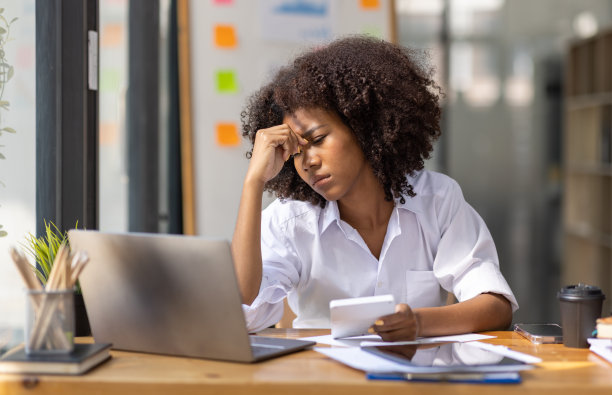 疲惫的年轻商业非裔美国妇女的肖像与文件税务笔记本电脑在办公室工作。悲伤，不快乐，担心，抑郁，或员工生活压力的概念图片下载