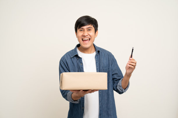 年轻兴奋的亚洲男子与许多包裹纸板站在孤立的白色背景。快乐的男子拿着许多包裹盒子从快递服务收到图片下载