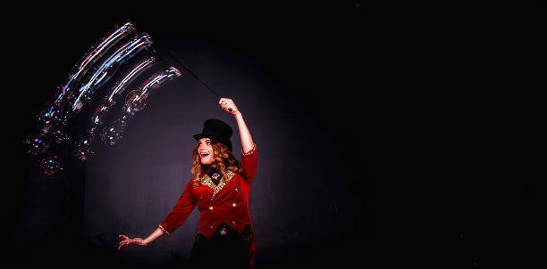 女魔术师做肥皂泡表演，一个魔术师在戏剧服装摆姿势在黑色背景。穿着舞台服装的女演员。戏剧表演和趣味表演的概念。复制广告文字空间图片下载