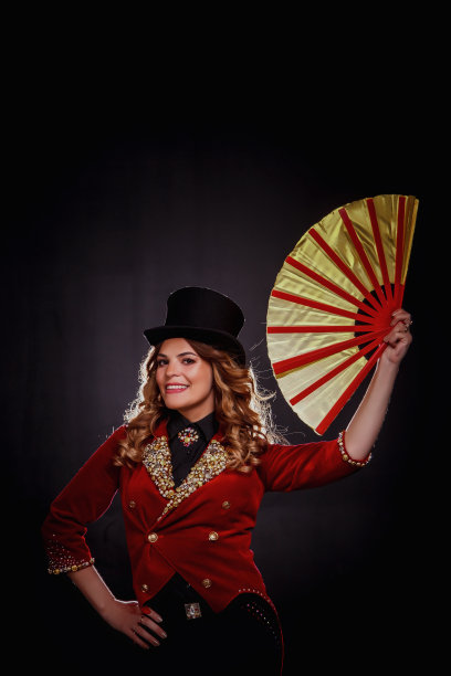女魔术师拿着东方扇子看着镜头，一名身穿马戏团服装的魔术师在黑色背景下表演。身着舞台服装的女演员。有趣表演的概念。复制广告文字空间图片下载