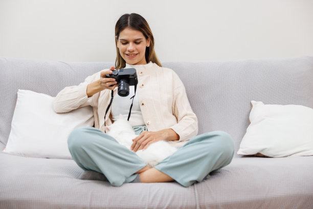 年轻女子坐在客厅的灰色沙发上和白色的波斯猫玩耍。亚洲摄影师正在拍摄波斯猫的照片。图片下载