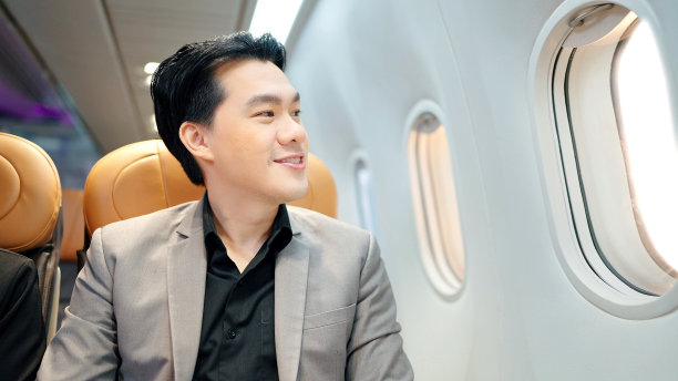 快乐的亚洲商人坐在飞机上，透过窗户往外看图片下载