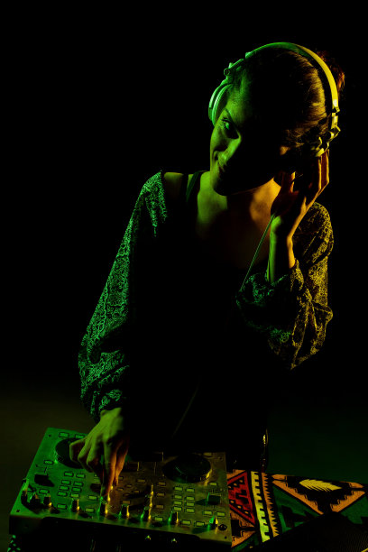 戴着耳机的女DJ。侧面点燃剪影的一个女孩玩电子音乐对黑色背景。图片下载