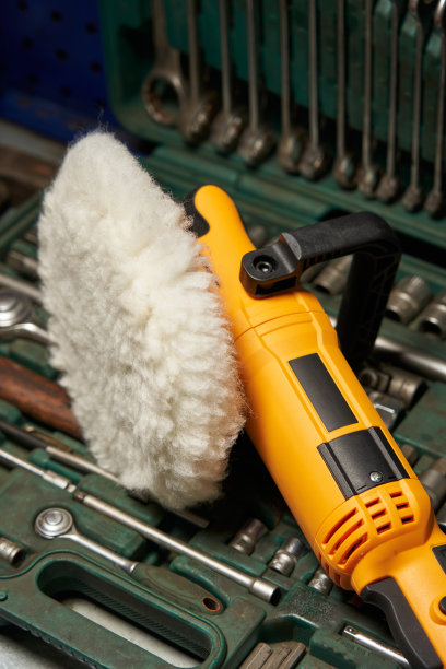 一个抛光角磨床的特写躺在一个绿色的手提箱与工具。一个蓬松的抛光头在上面。箱子里有钥匙、头、锤子、拨浪鼓。图片下载