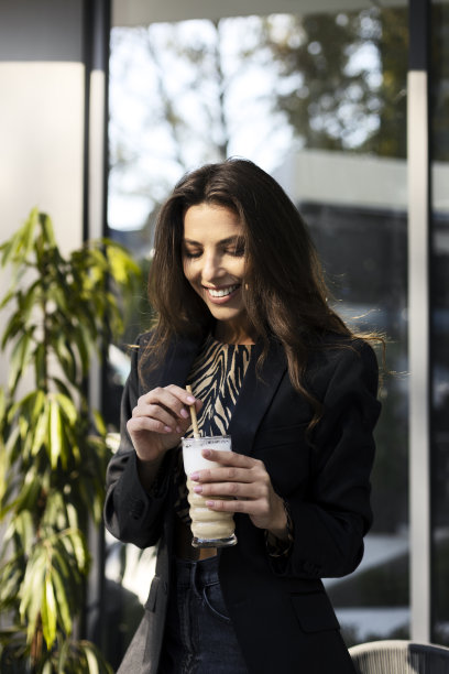 一个美丽的，微笑的女孩的肖像，拿着一杯咖啡饮料在她的手中。咖啡馆里的年轻女子。图片下载