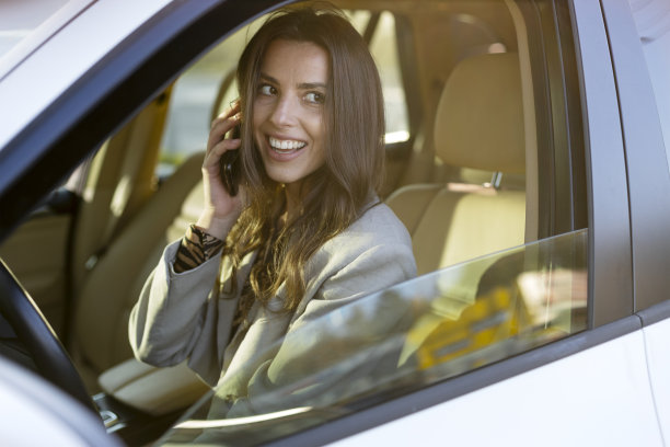 迷人的女商人一边开车一边讲智能手机。开车时打电话。图片下载