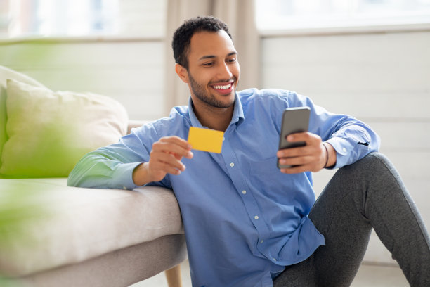 微笑的阿拉伯男子在家使用手机和信用卡图片下载