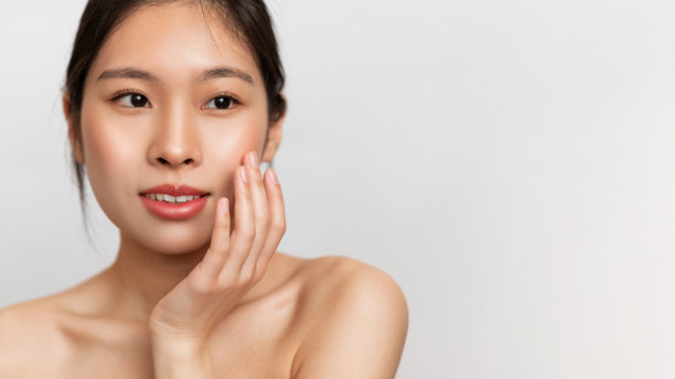 感性的韩国女士触摸面部和微笑的柔软皮肤的肖像，白色的工作室背景，全景，自由空间图片下载