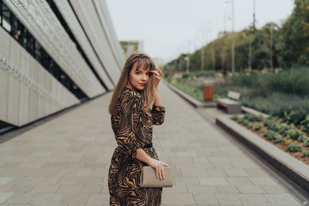 年轻女子走着，回头看，穿着裙子，拿着她的包/钱包图片下载