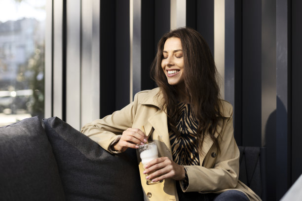 梦幻的女孩闭上眼睛，手里拿着一杯饮料，坐在咖啡馆柔软的沙发上。小女孩下班后休息。图片下载