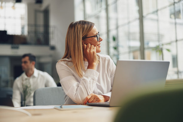 女性自由职业者在笔记本电脑上工作，在同事的背景下共同工作，看着窗户图片下载