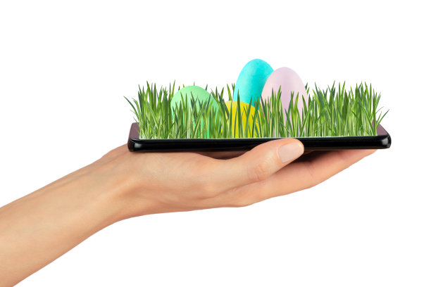 智能手机放在女性手掌上。新鲜的草地和从手机屏幕上伸出来的彩绘彩蛋。网上购物创意，节日促销应用，手机问候图片下载