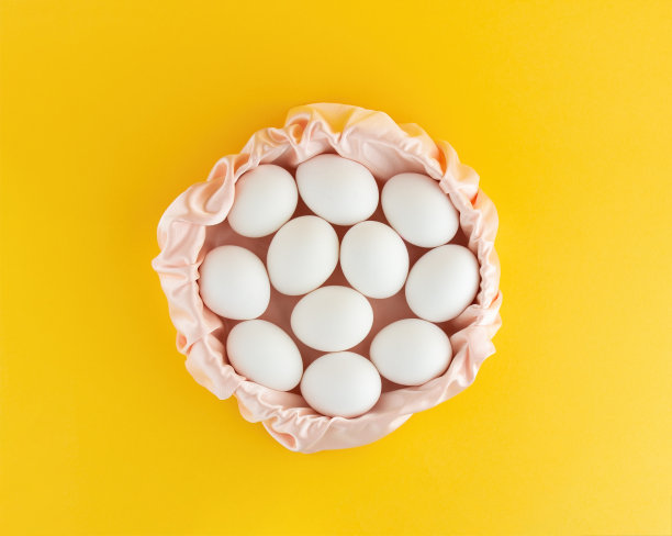白色的鸡蛋躺在黄色背景的粉色丝绸篮子里。复活节作文，大量空白图片下载