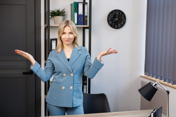 时尚迷人的年轻金发女商人站在办公室的桌子旁边看着相机可爱的微笑图片下载