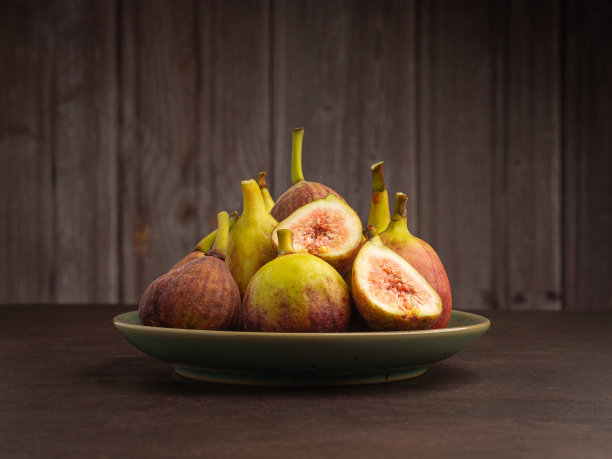 在以木墙为背景的复古地板上，盘子里放着一堆成熟的无花果。图片下载