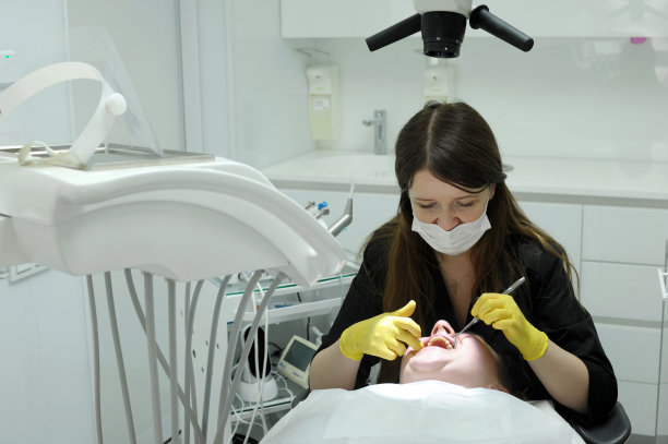 女牙医戴着黄色手套和黑色衣服，她在镜子的帮助下检查病人的假牙，白色背景的现代牙医办公室的最新技术很多图片下载