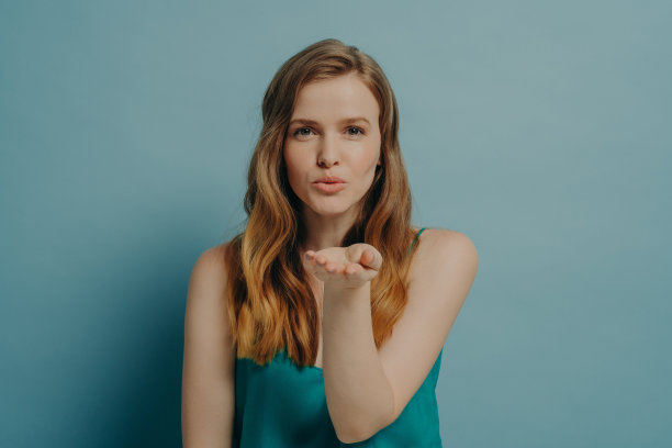 漂亮坦率的女孩吹飞吻和表达爱，而孤立地站在蓝色的背景图片下载